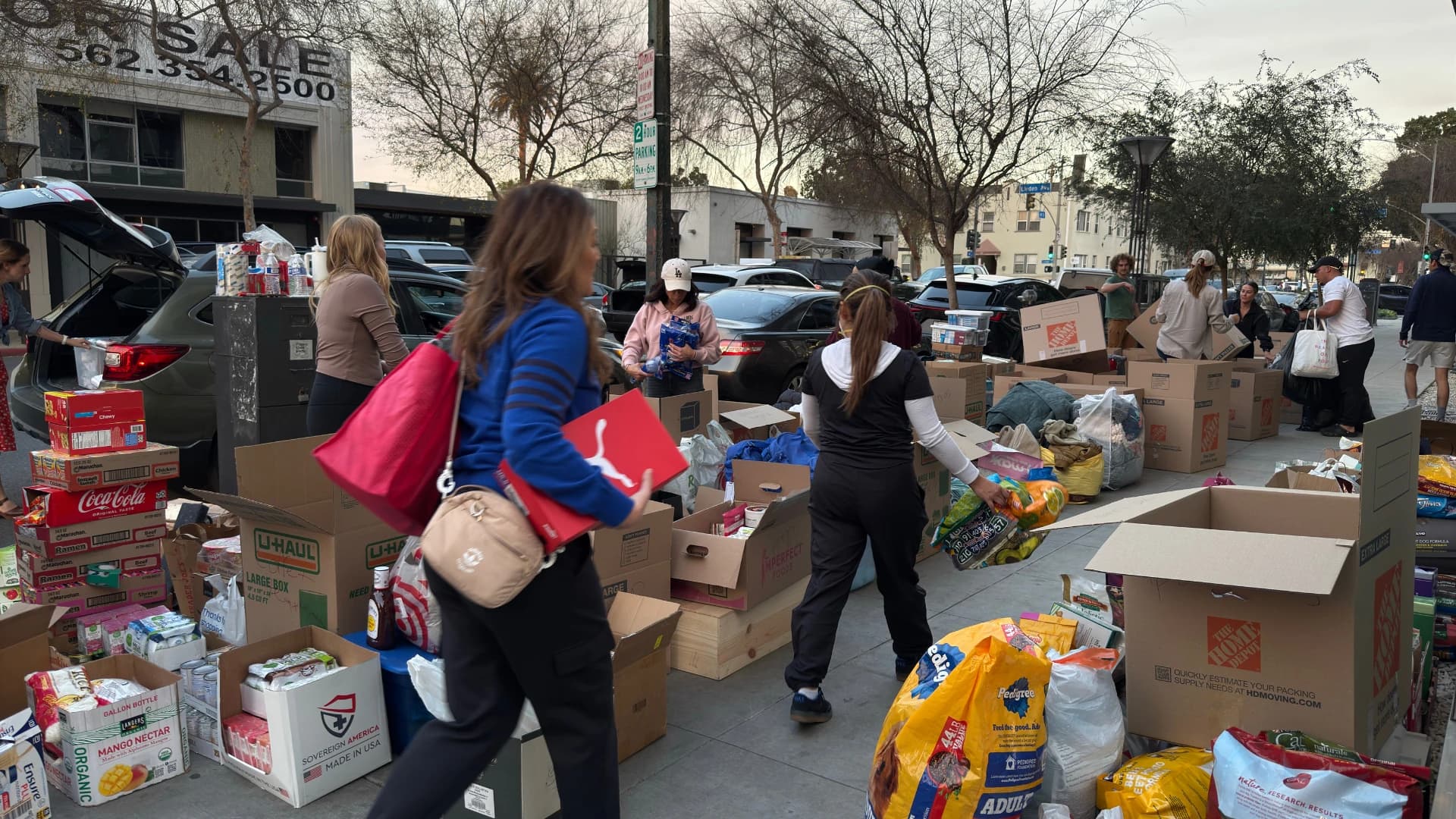 Boxes of donations lining the sidewalk as volunteers carry supplies toward the U-Haul